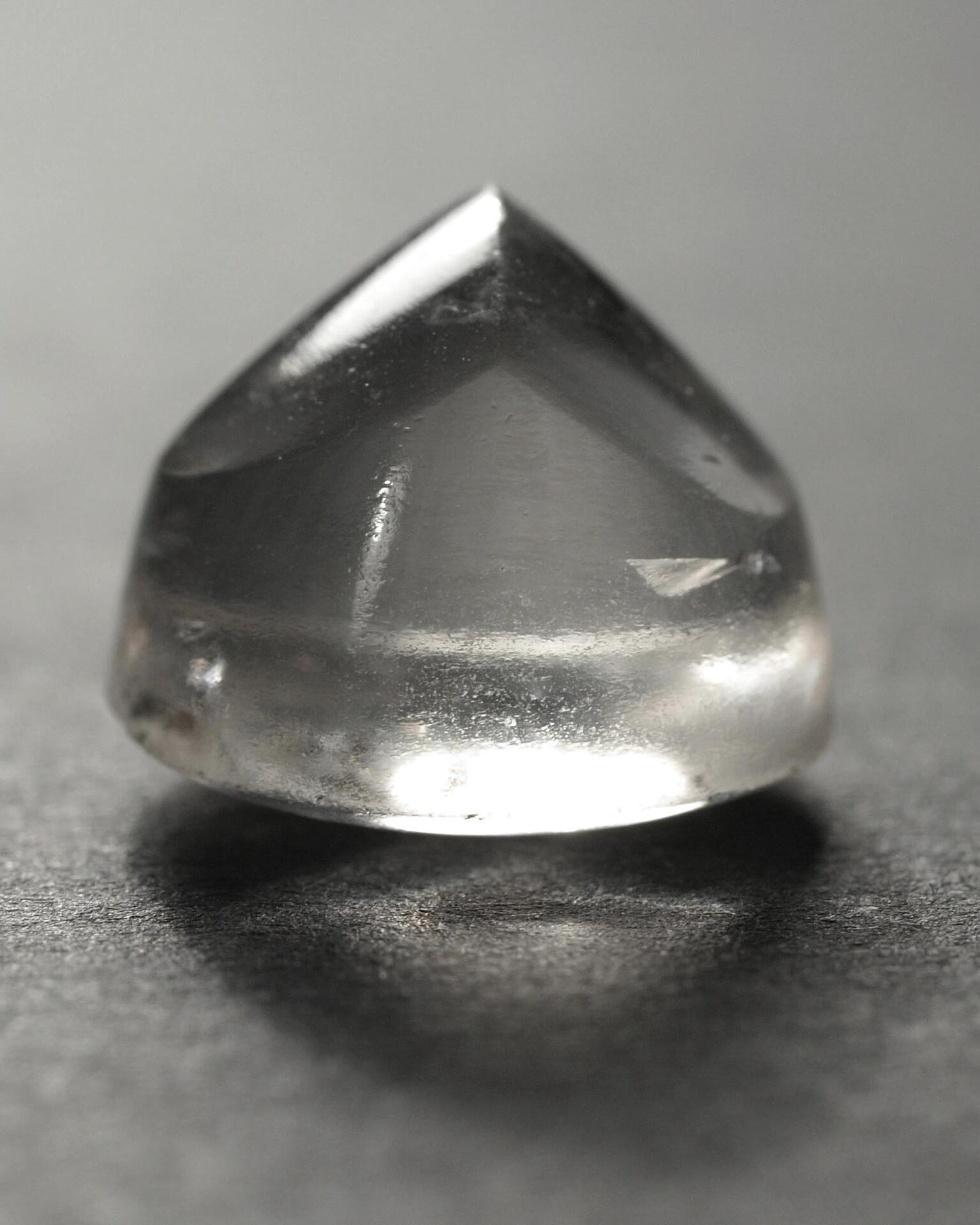 Photo of a transparent, slightly rough crystal piece with round bottom and crested top.