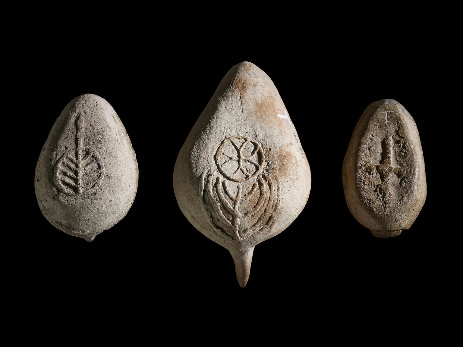 Photo of three clay teardrop-shaped objects with symbols, including a ritual candelabrum.