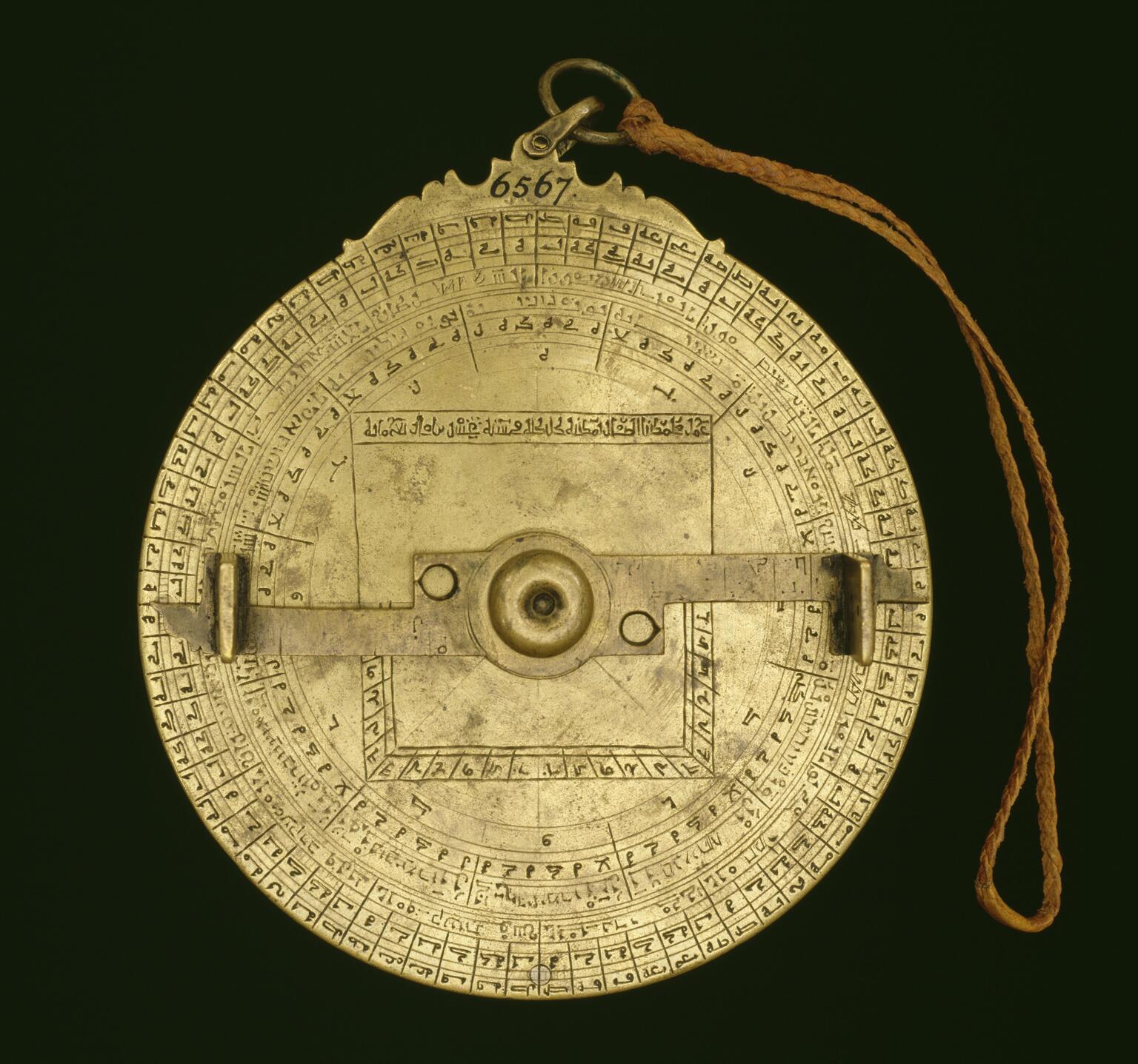 Circular, intricate brass object with Arabic and Hebrew inscriptions, geometric markings, and a rotating arm.