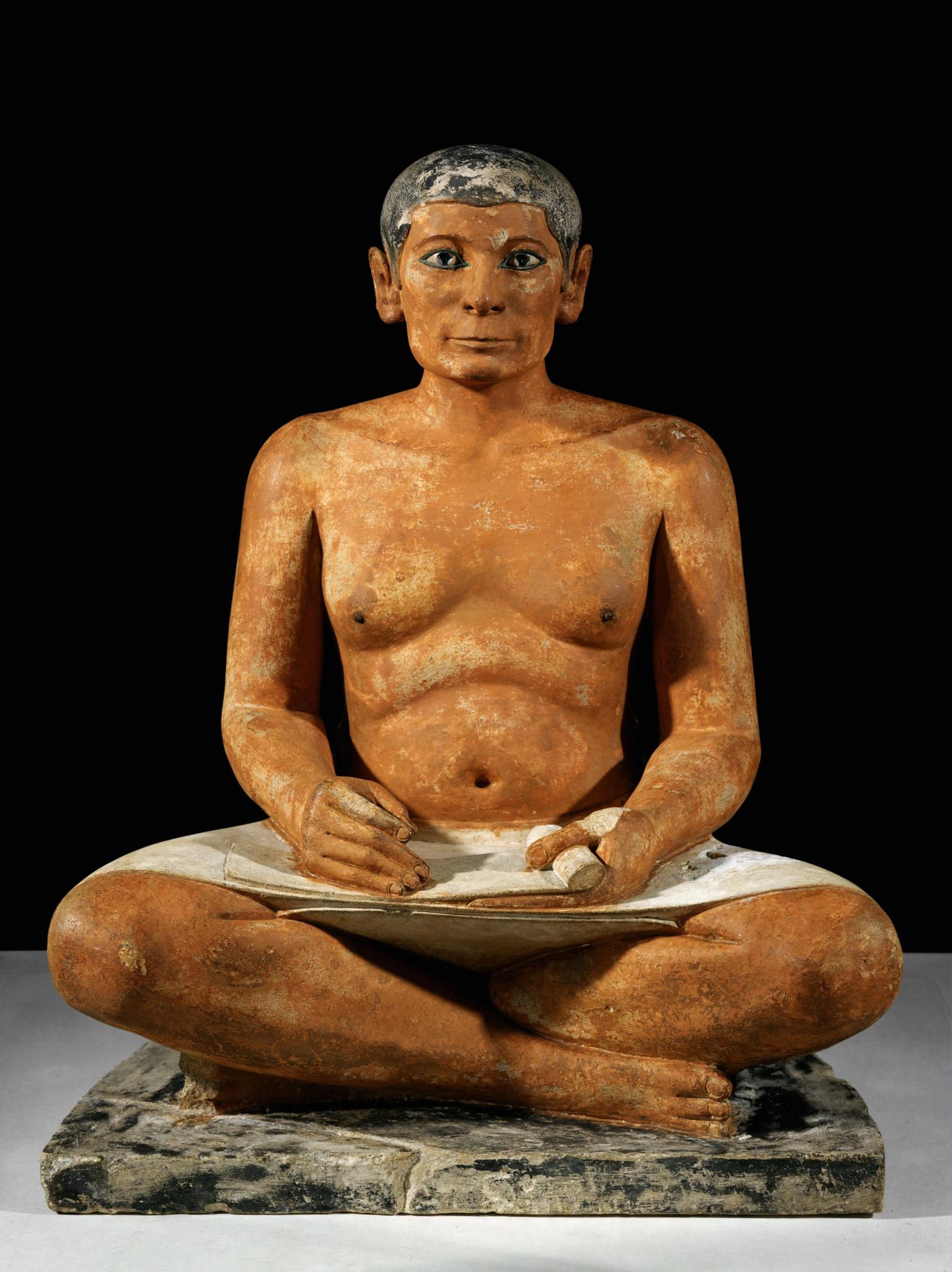 Sculpture of man sitting cross legged with scroll in his lap.