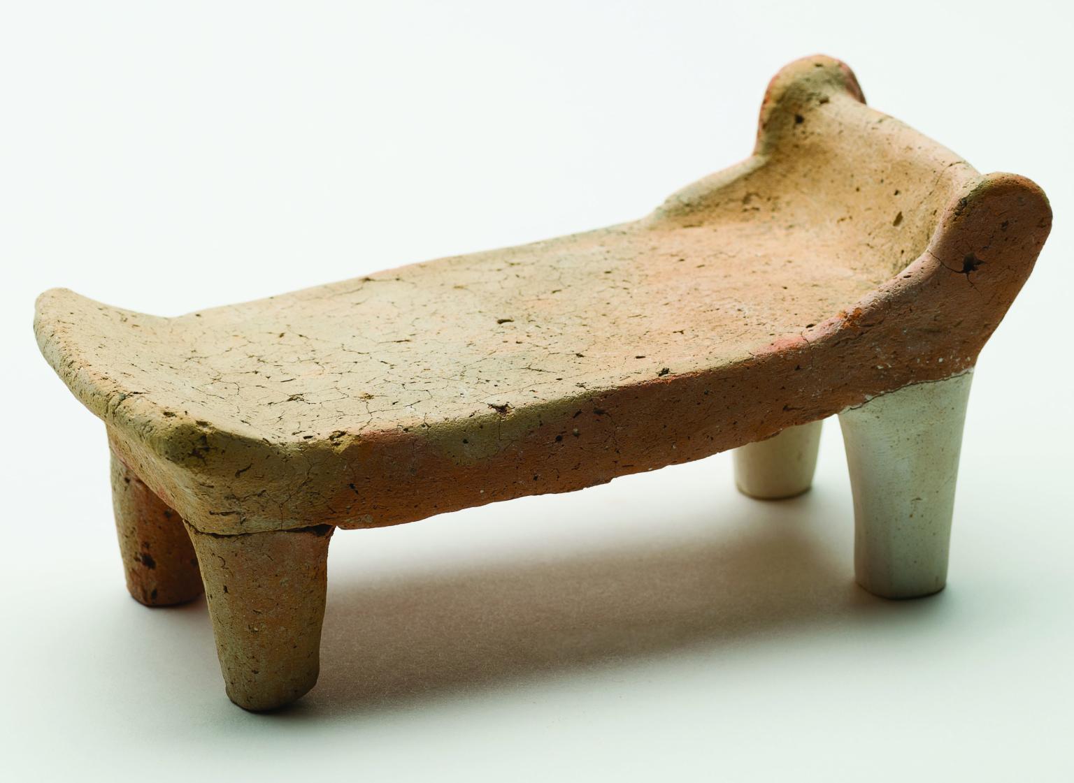 Terra-cotta bed with headrest and footrest standing on four legs.