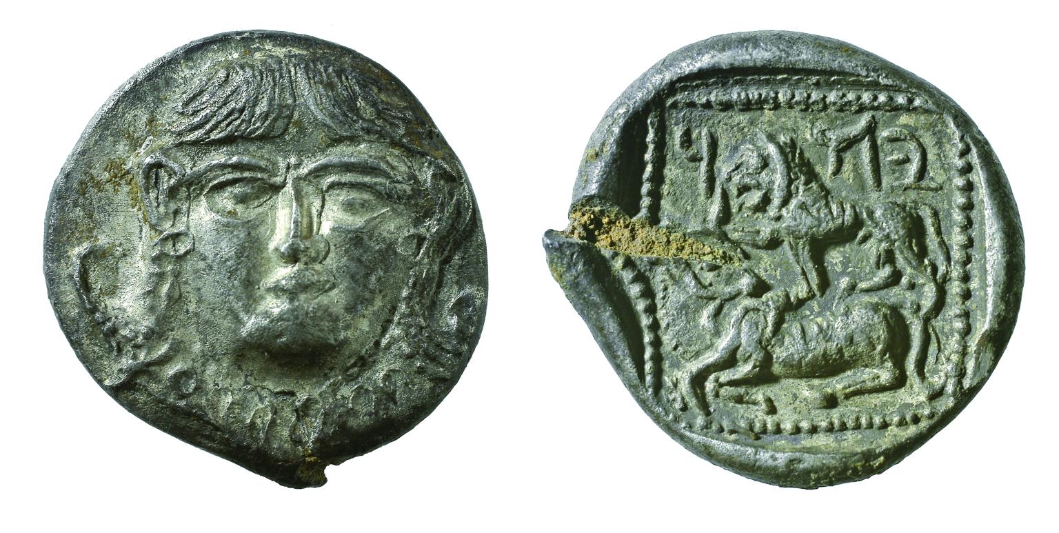 Front and back of coin, with image of face on front of coin and lion, bovine, and Hebrew inscription on back.