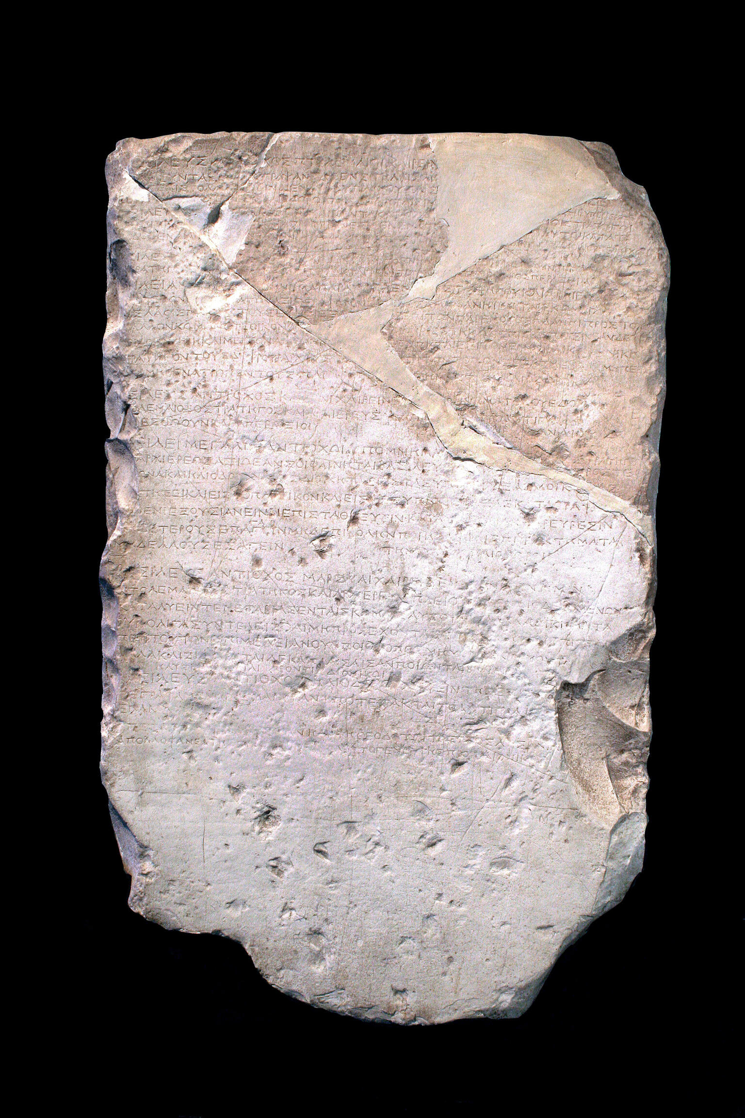 A weathered, roughly rectangular stone slab with ancient Greek inscriptions carved into its surface. Several parts are chipped, cracked, and uneven, with some repairs visible.