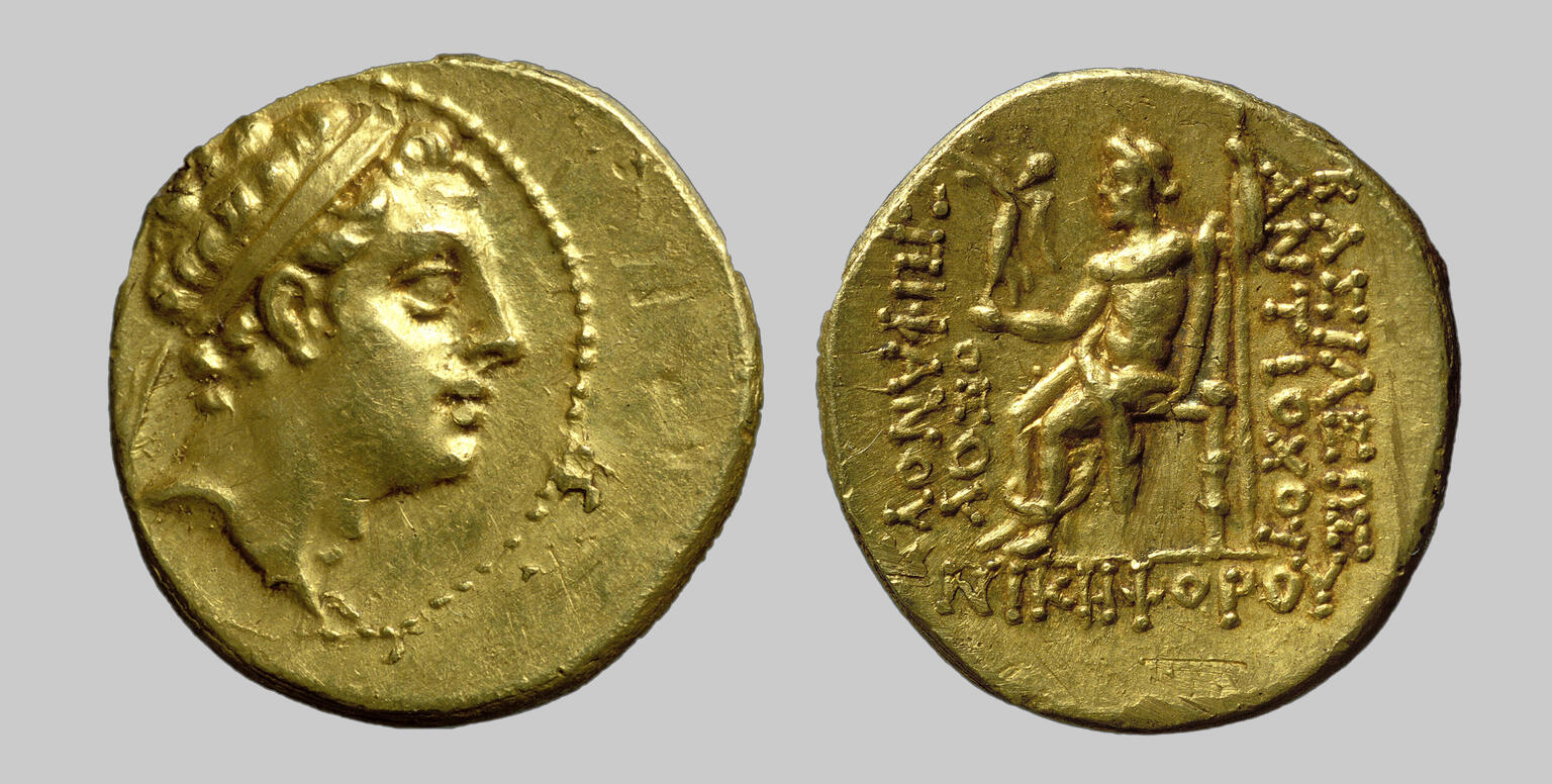 Ancient gold coin. Obverse shows a right-facing profile with a diadem. Reverse depicts a seated figure holding an object, surrounded by inscriptions in Greek.
