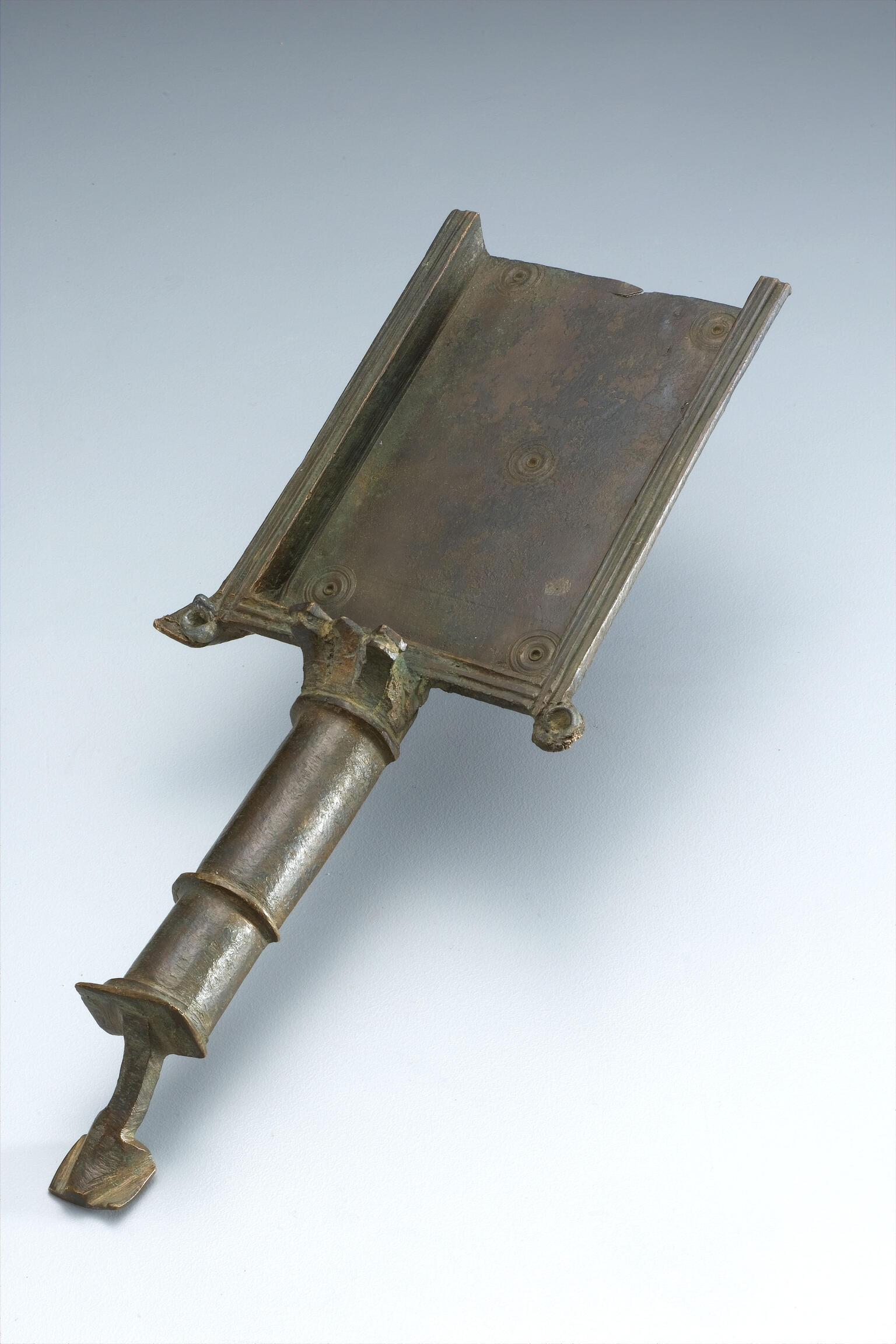 Ancient bronze shovel with a rectangular surface and a tapered cylindrical handle.