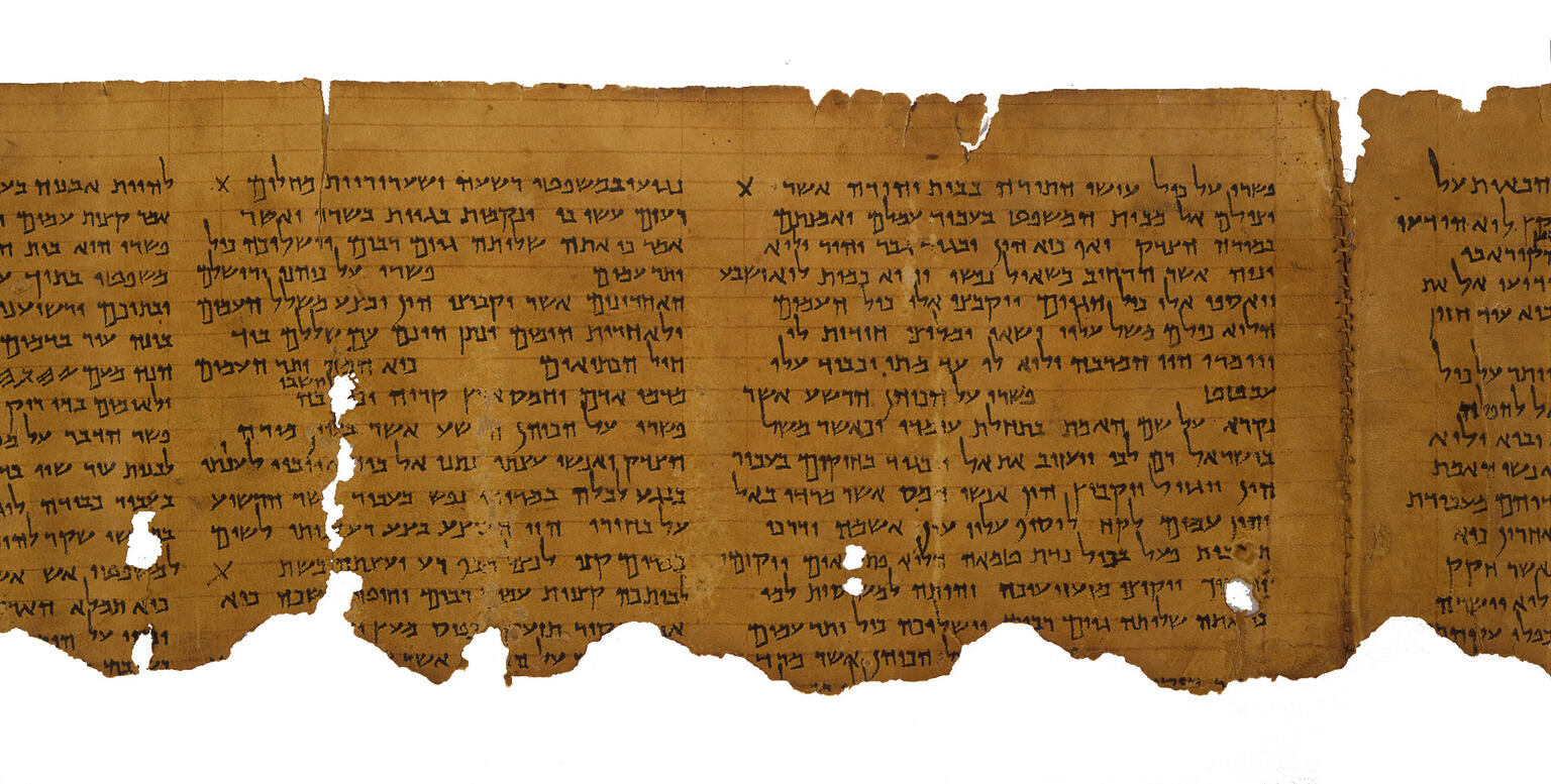 A fragment of an ancient, weathered scroll with rows of Hebrew text. The parchment edges are torn and uneven, showing signs of age and wear.