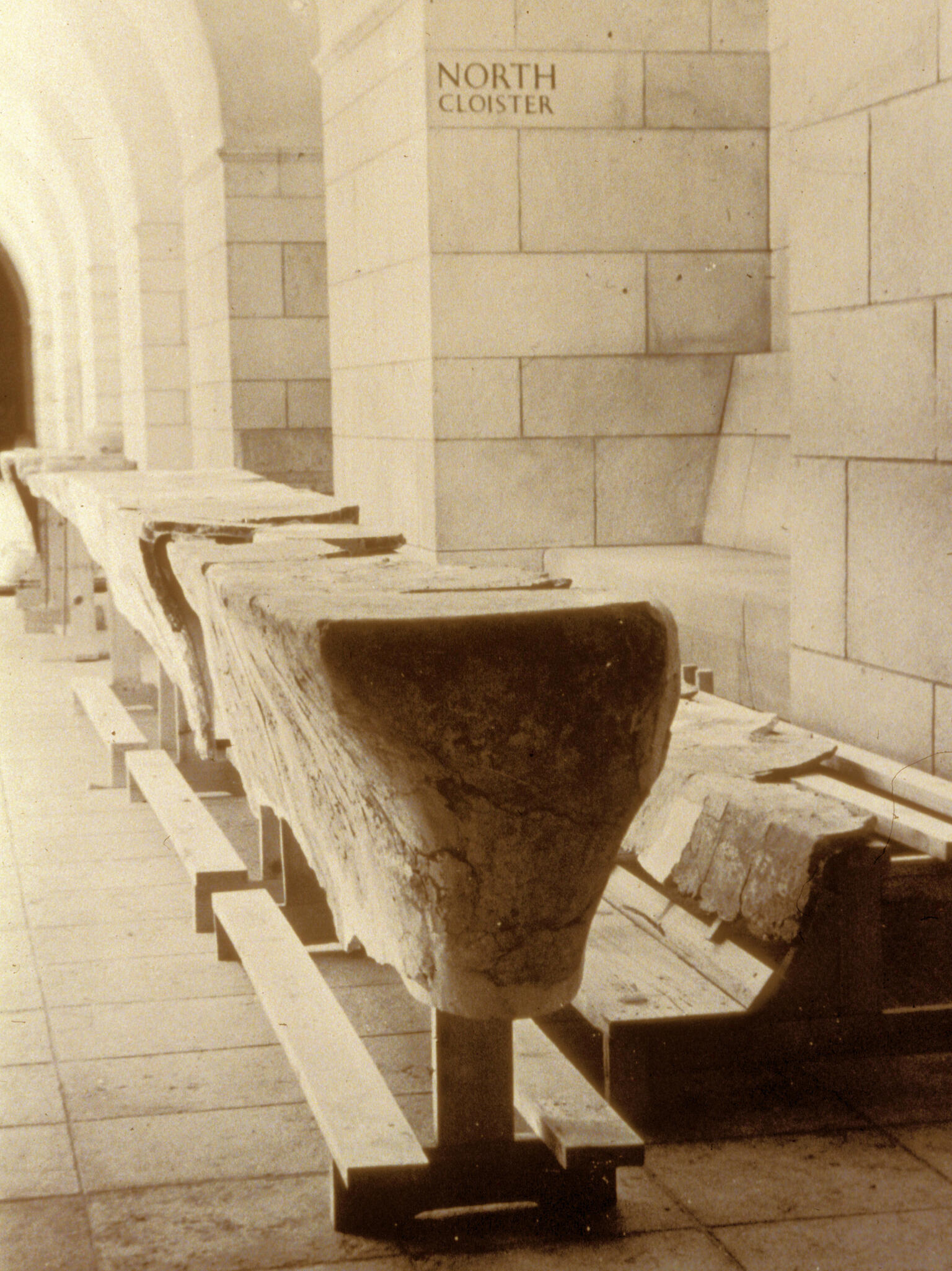 Wooden supports in the shape of a long, narrow table and bench with slabs of broken plaster on top, in a room with arched ceilings and stone walls.