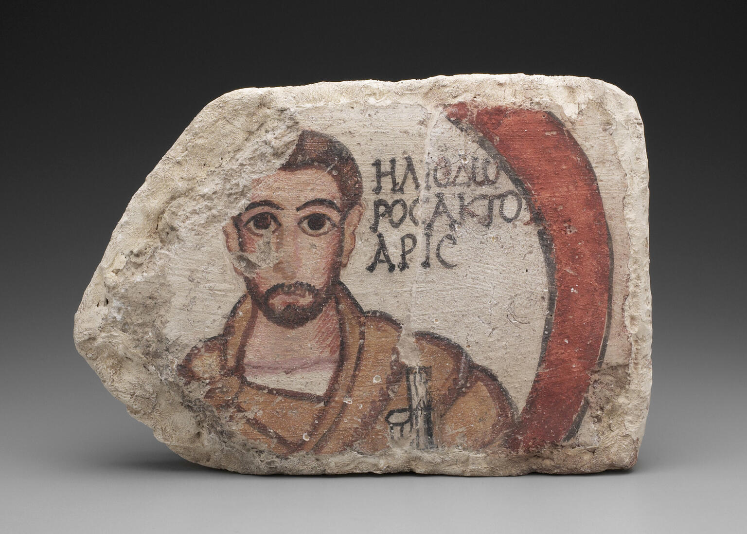 Ancient clay block with painted plaster featuring a bearded man with large eyes, wearing a brown robe, next to Greek text and a red curved shape.