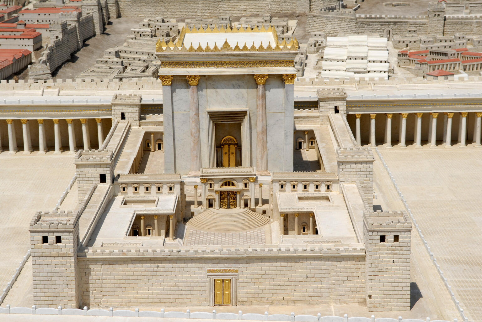 A detailed model of a temple, featuring stone walls, columns, golden accents, and surrounding courtyards, with other structures visible in the background.