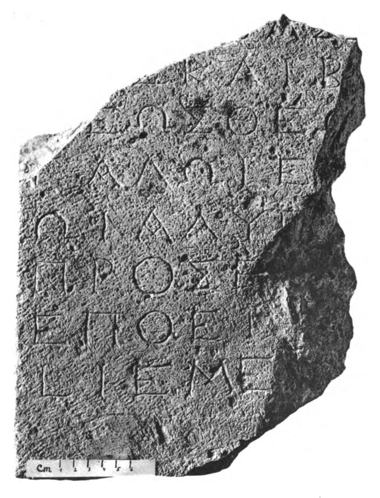 A stone fragment inscribed with ancient Greek text in several lines. The edges are irregular and broken.