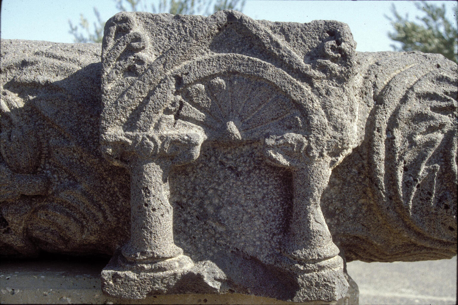 Weathered stone carving featuring two short columns supporting an arch with a fan-like design inside.