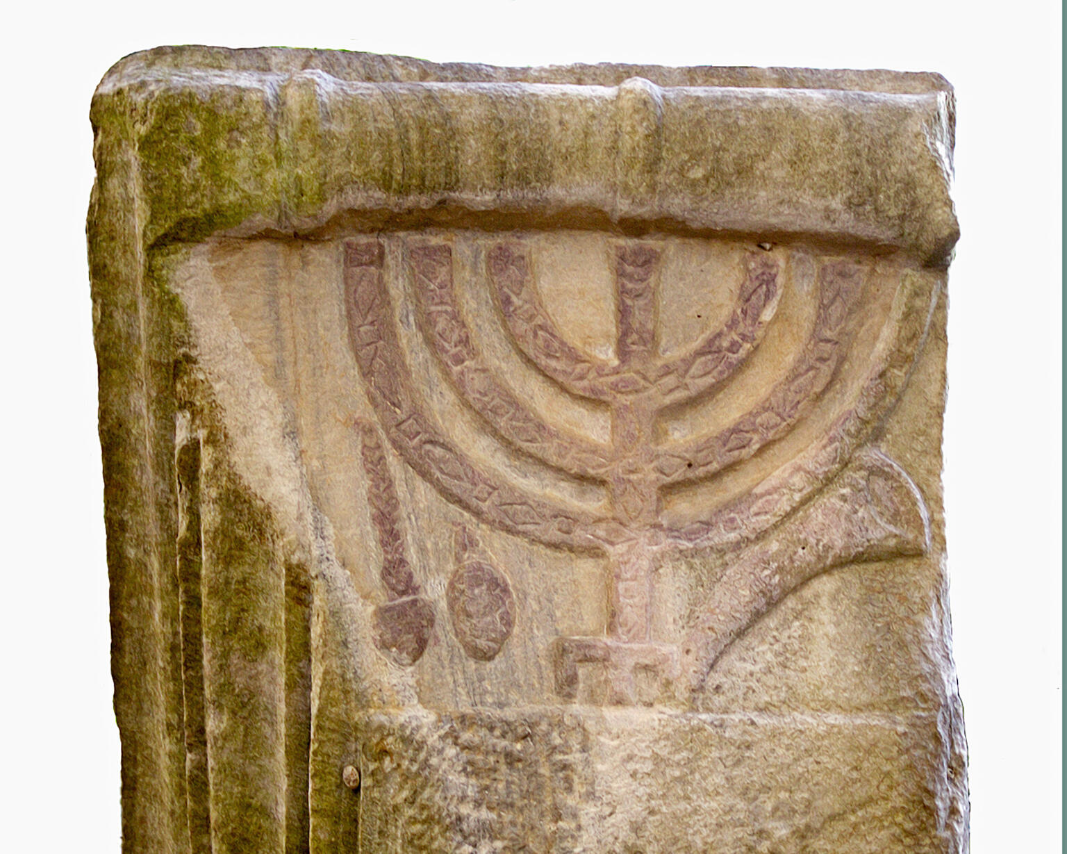 Ancient worn and weathered stone relief featuring a menorah and other symbols against a plain background.