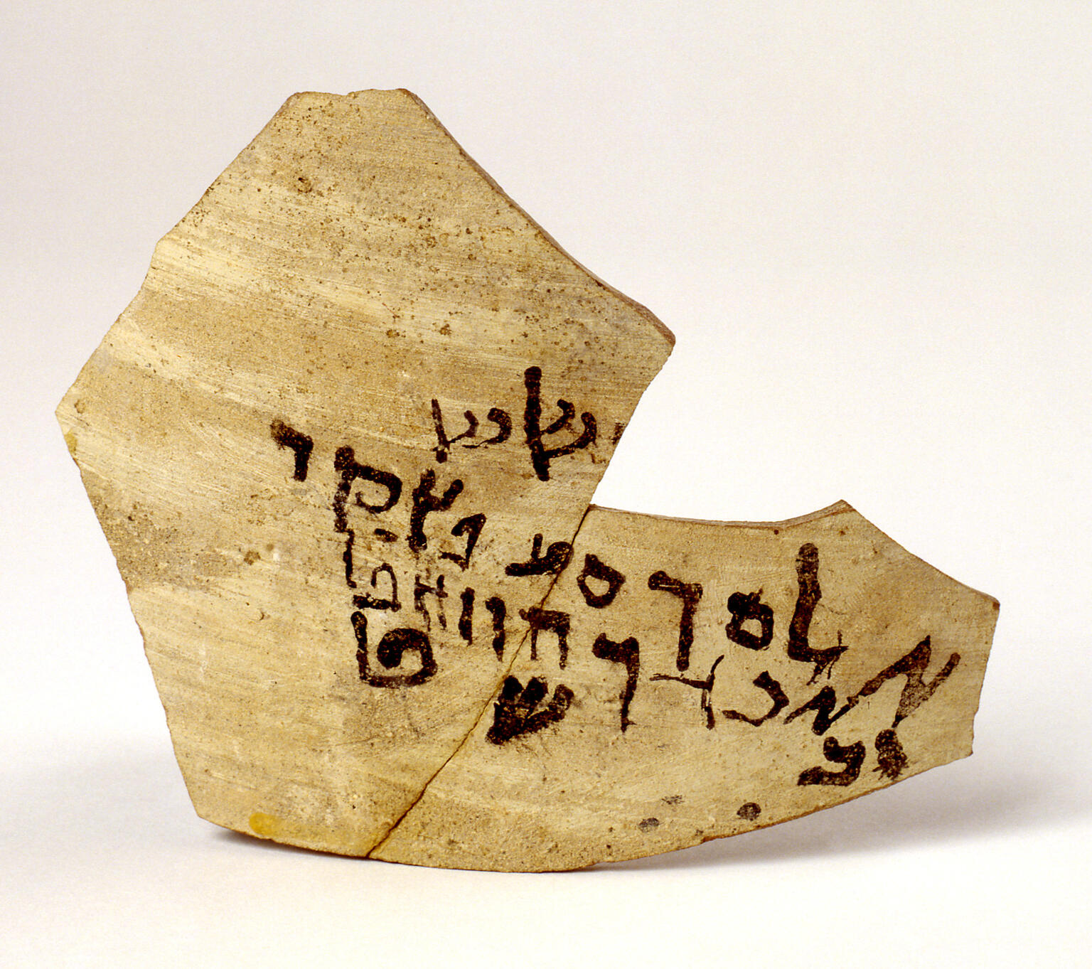 A broken piece of pottery with ancient Hebrew script written in black ink across its surface.