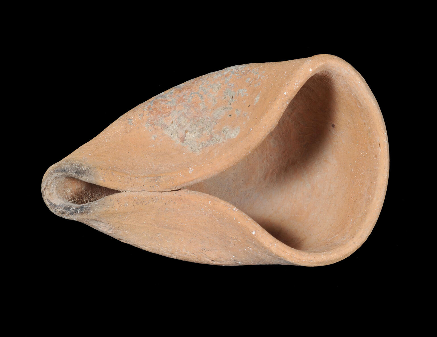 A clay oil lamp with a wide, rounded body and a pointed spout, showing surface wear and some discoloration.