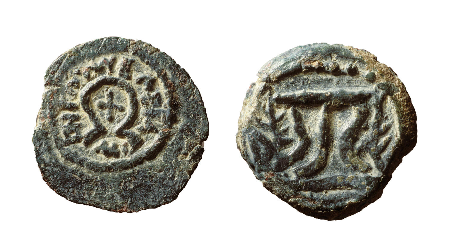 Two sides of an ancient, weathered coin: one side shows an x shape surrounded by an omega shape, encircled by Greek inscriptions, and the other features a tripod flanked by branches. The metal is rough and greenish.