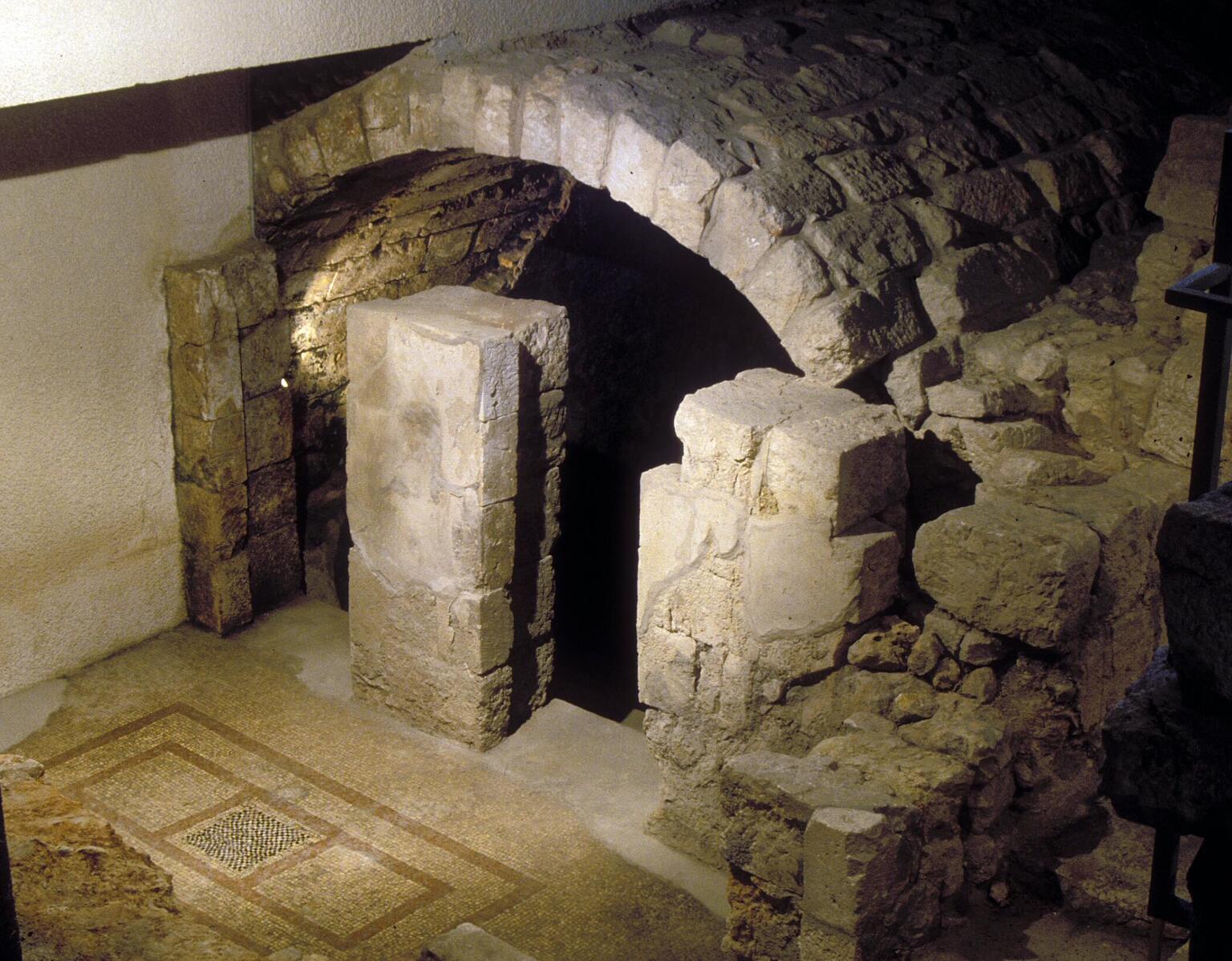 Stone archway surrounded by partially built stone structures, with tile mosaic visible on the floor next to the archway.