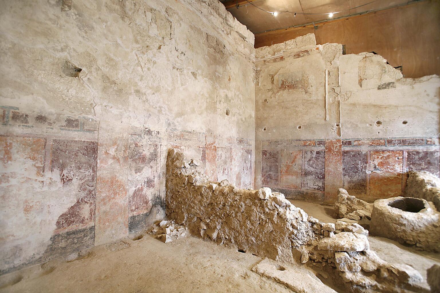 Ancient, weathered room with faded wall paintings, exposed stone walls, and a rough stone structure in the center.