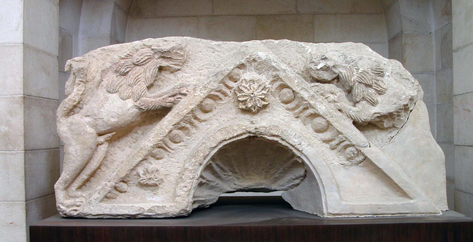 A weathered stone fragment featuring two carved lions surrounding a triangular roof with an arched opening.