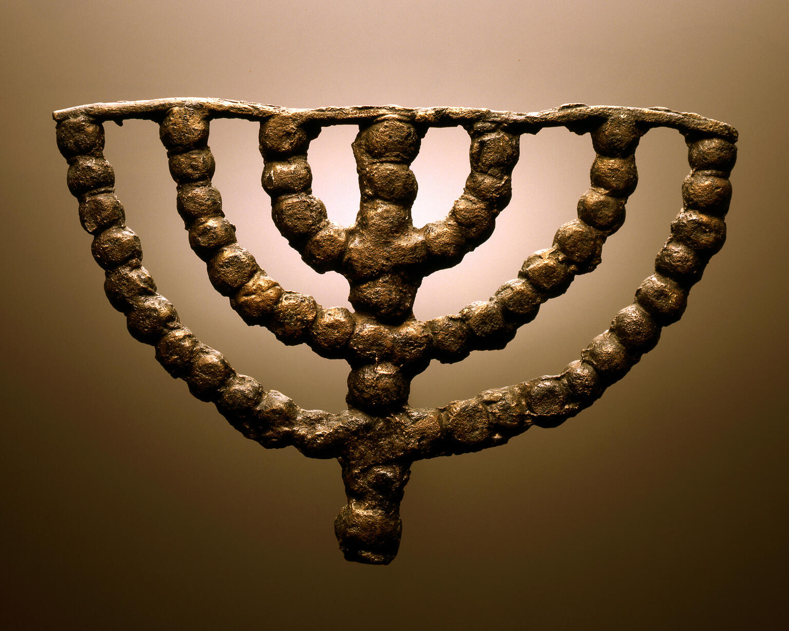 Ancient bronze menorah with seven branches, crafted from round beads forming its shape.
