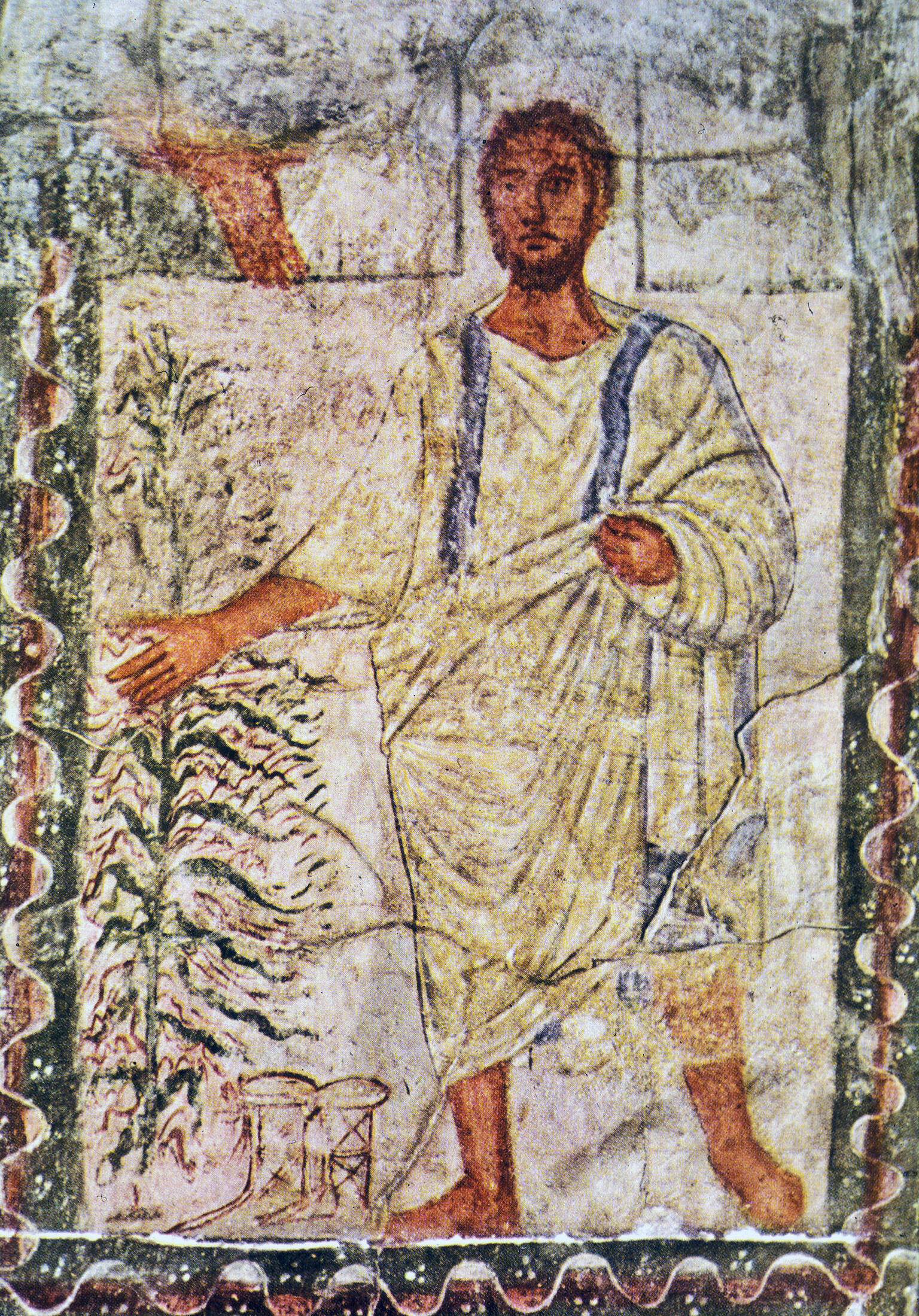 Ancient fresco of a bearded man in a white robe with blue stripes, standing beside a leafy bush, with his right arm extended and left hand holding his garment. The background shows architectural details and faded colors.