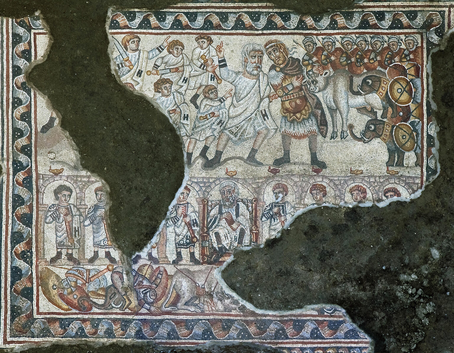 Ancient mosaic depicting armed soldiers, a group of robed figures, and battle elephants, surrounded by a decorative border. Some details are obscured by damage.