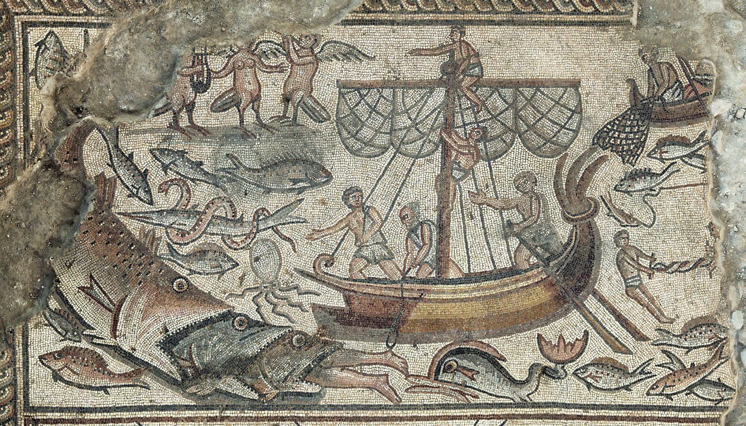 Ancient mosaic depicting a ship surrounded by sea creatures, including large fish, with sailors on board and figures in the water; some mythological beings and decorative details are visible.