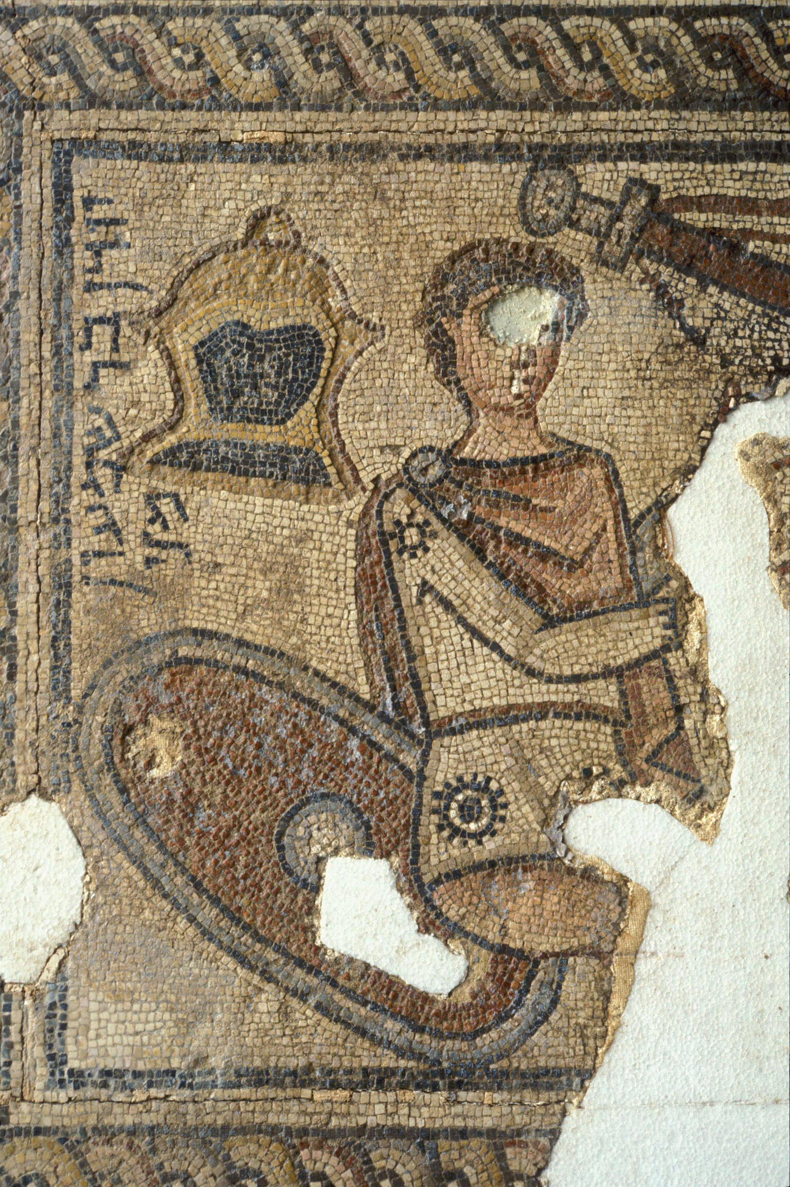Ancient mosaic depicting a partially damaged figure in armor, with a helmet, shield, and sword in the background. Some areas of the mosaic are missing.