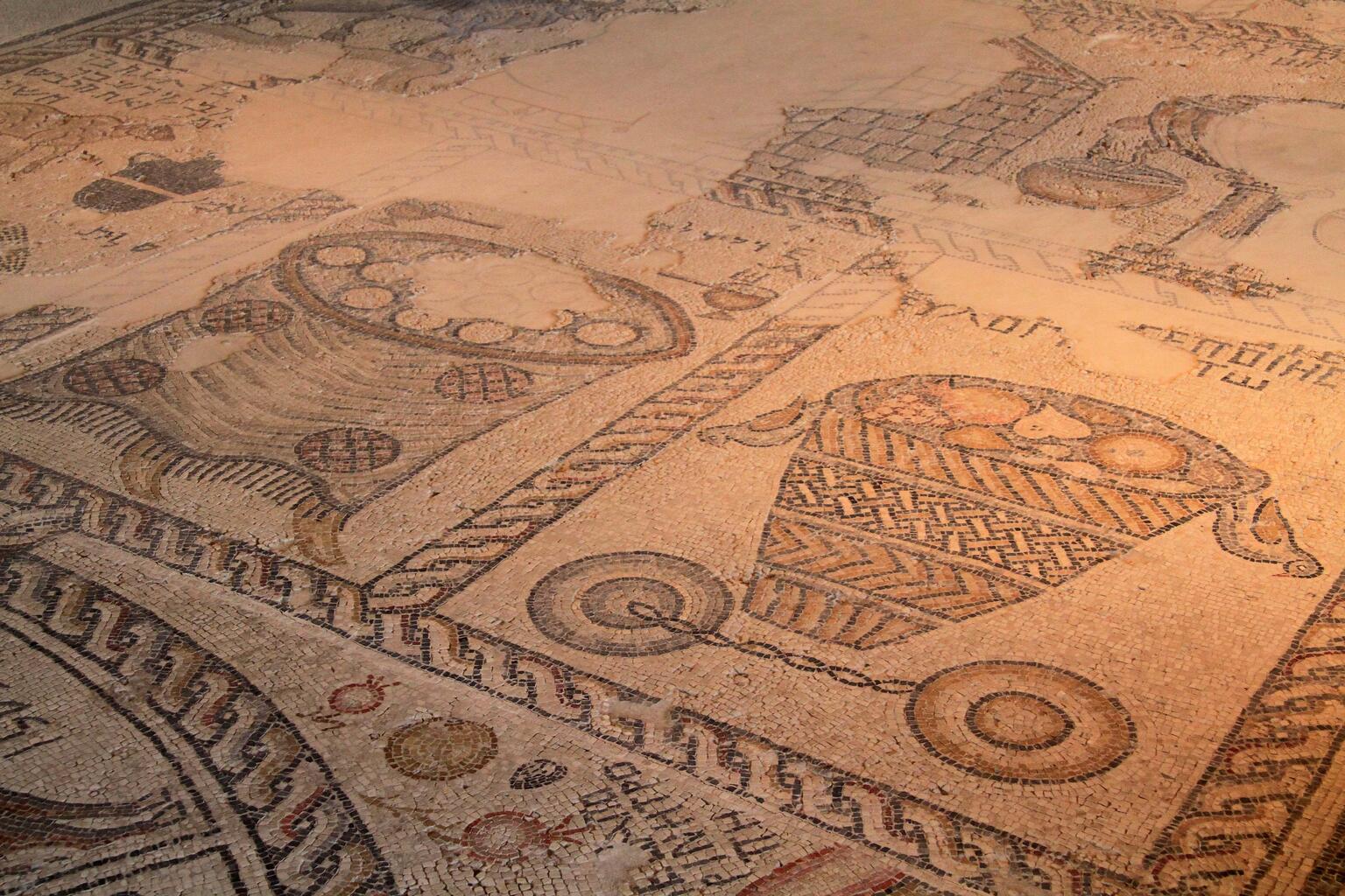 Ancient mosaic floor showing a basket filled with fruit with two birds hanging off it, and other items, surrounded by decorative borders.