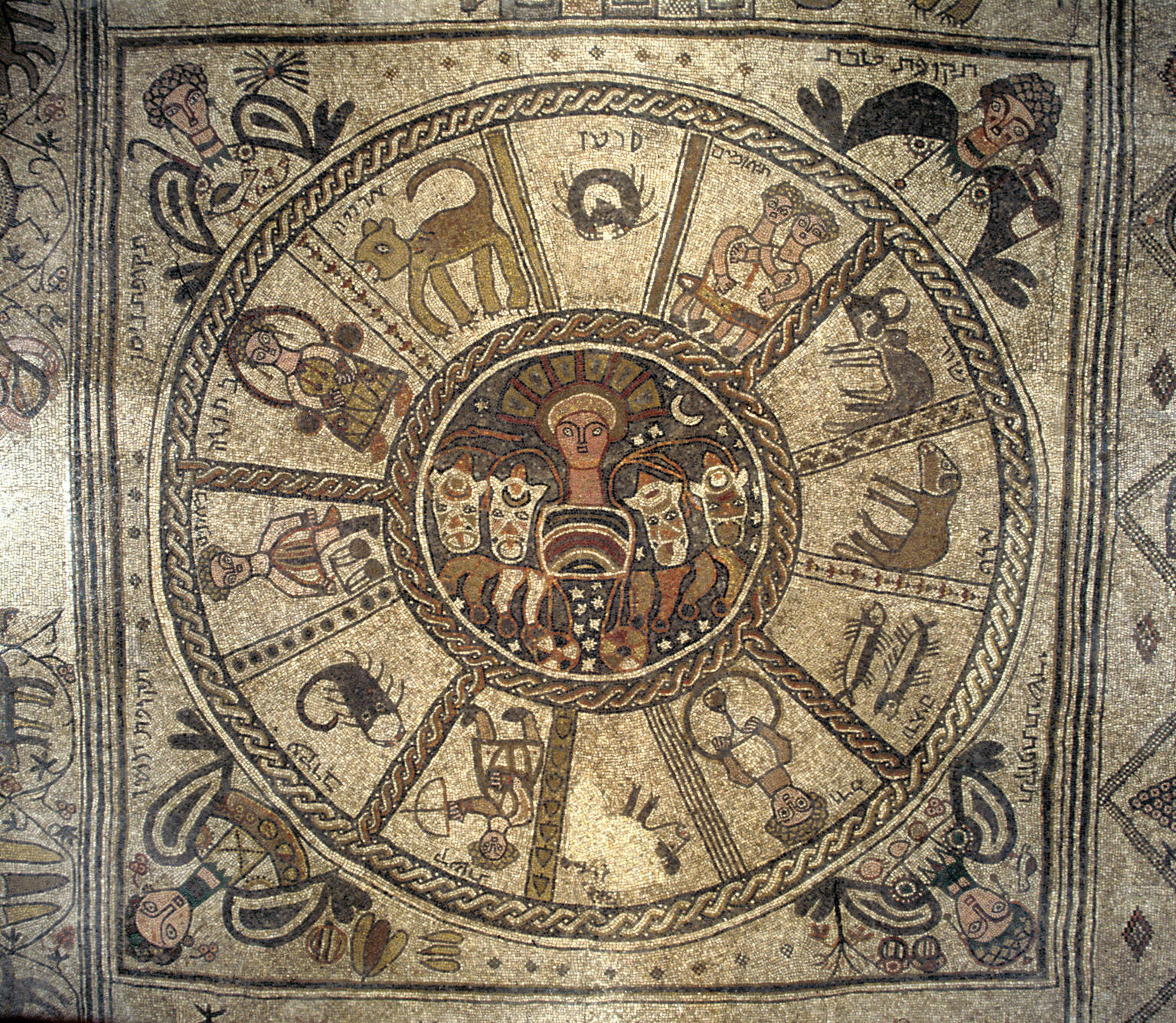 Ancient mosaic featuring a central figure surrounded by twelve sections, each depicting a zodiac sign with symbolic animals or figures, bordered by decorative patterns and human faces.