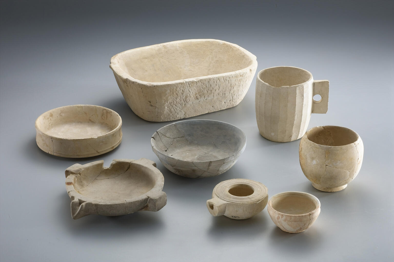 Six ancient ceramic jars and vessels of varying sizes and shapes, some with visible repairs, are arranged in two rows.