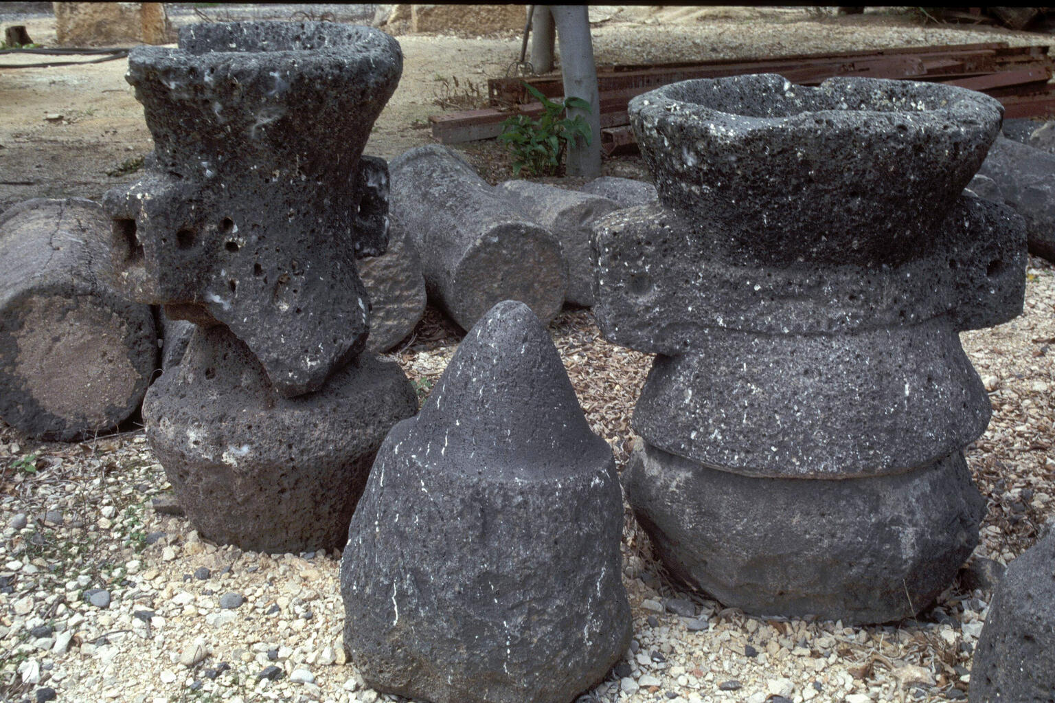 Several large, weathered grindstones are grouped outdoors on gravel.