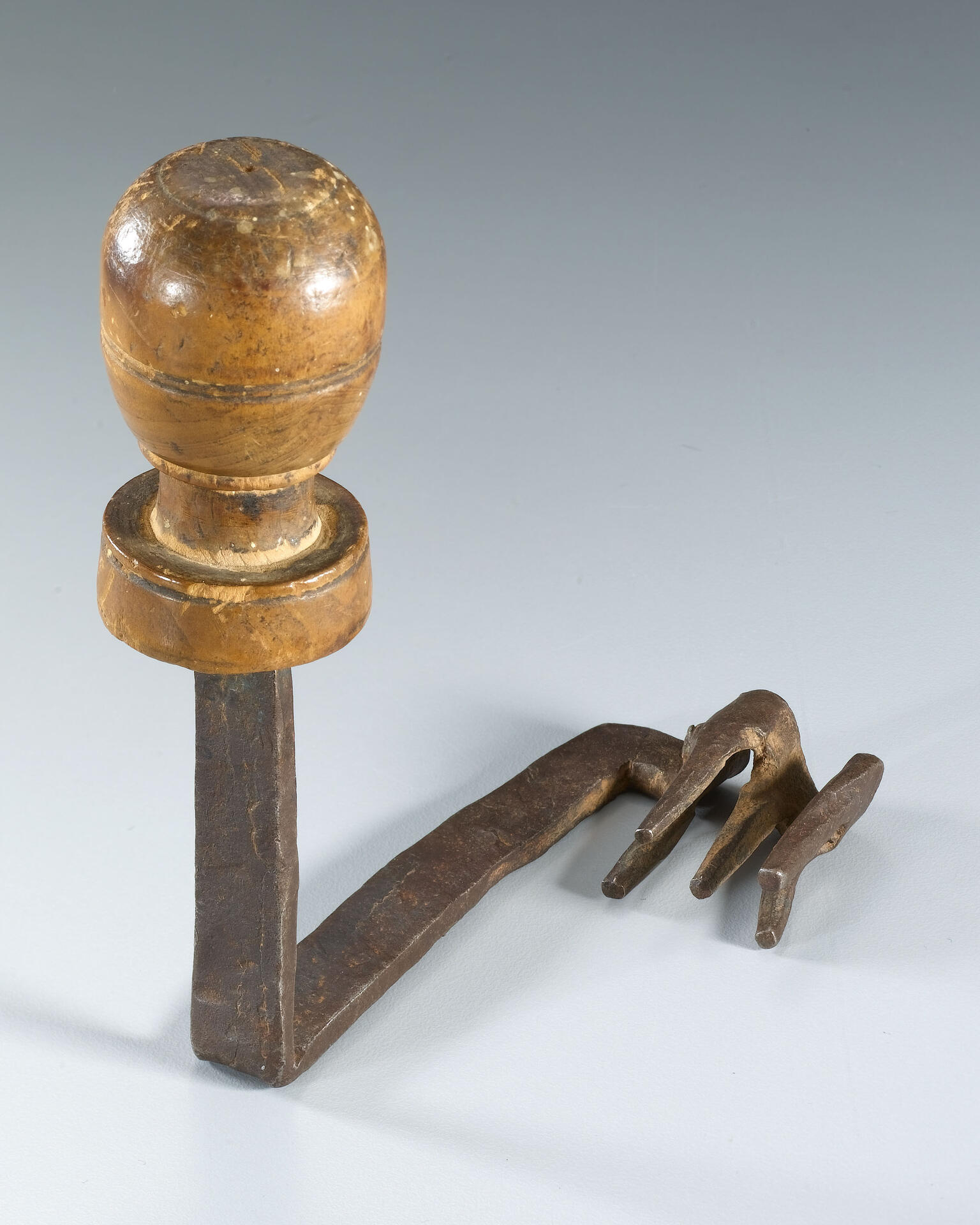 An object with a round wooden handle and a metal shaft ending in prongs resembling a claw.