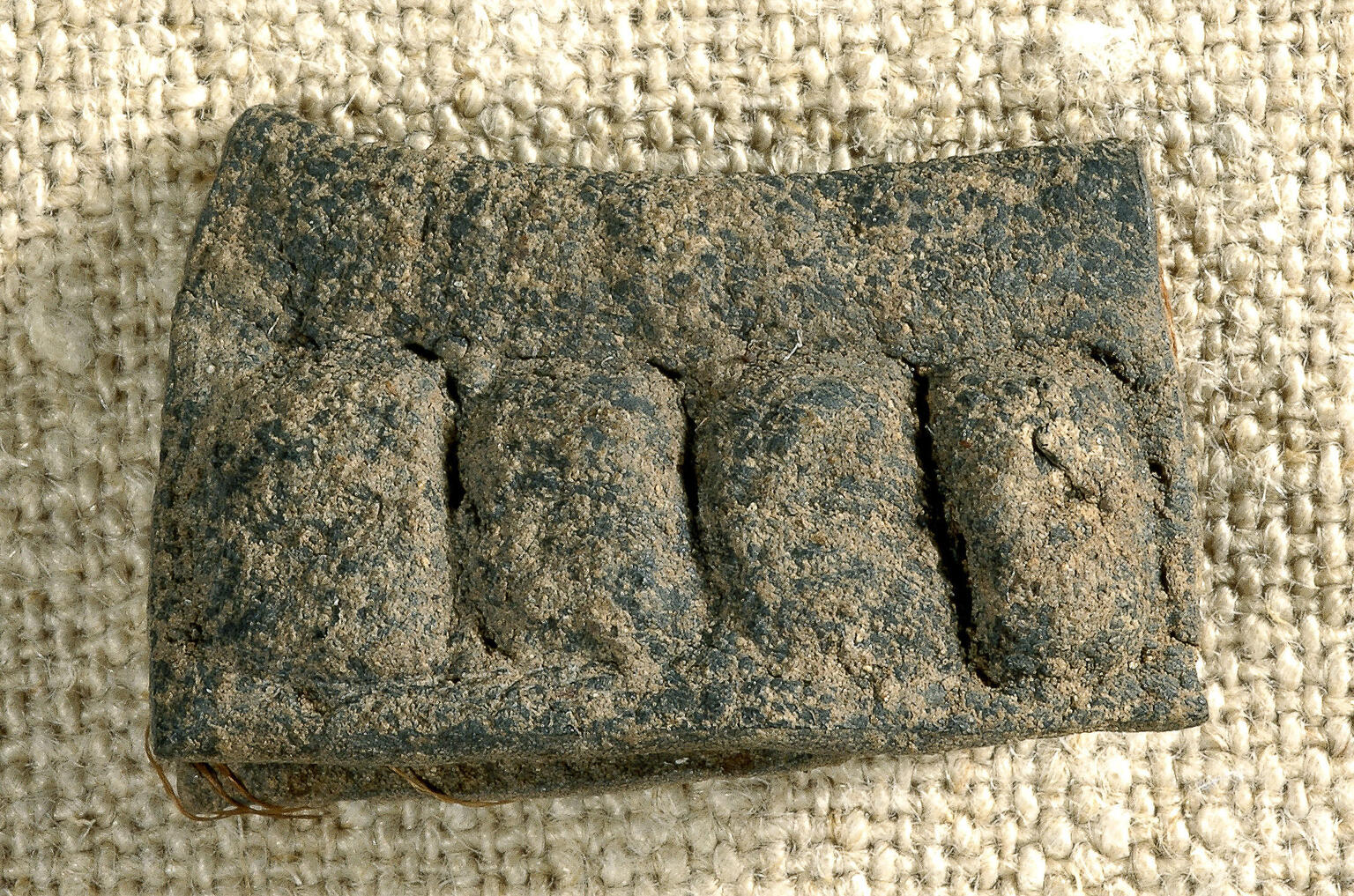 A rectangular, weathered artifact with four raised, rounded sections sits on coarse fabric.