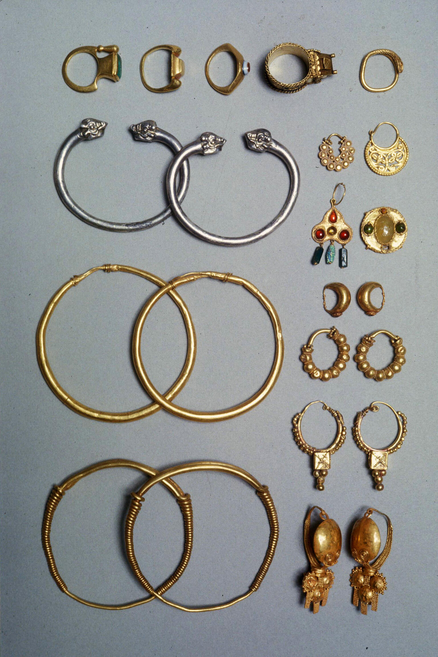 A collection of ancient jewelry, including rings, earrings, and bangles in various sizes and designs, made of gold and silver, some with gemstones.