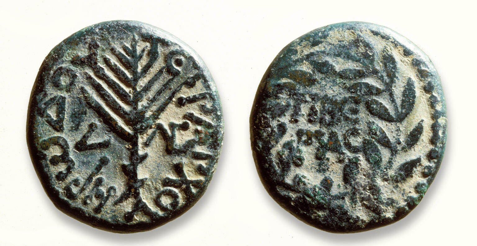 Two sides of an ancient bronze coin: one shows a stylized palm branch surrounded by Greek text, and the other has a wreath with Greek text inside.