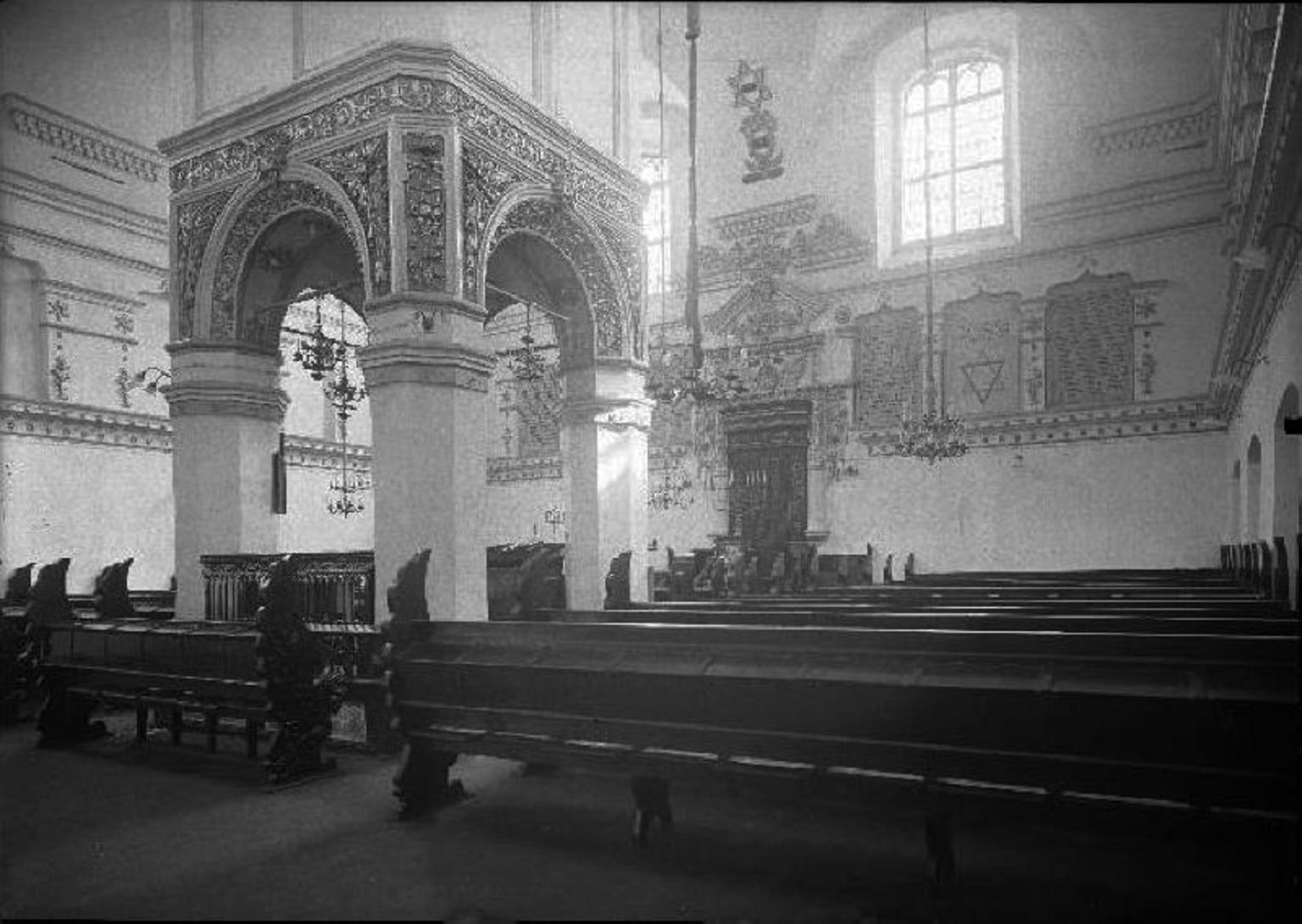 Photograph of building with central canopied platform, rows of benches, and ornate Torah ark on back wall. 