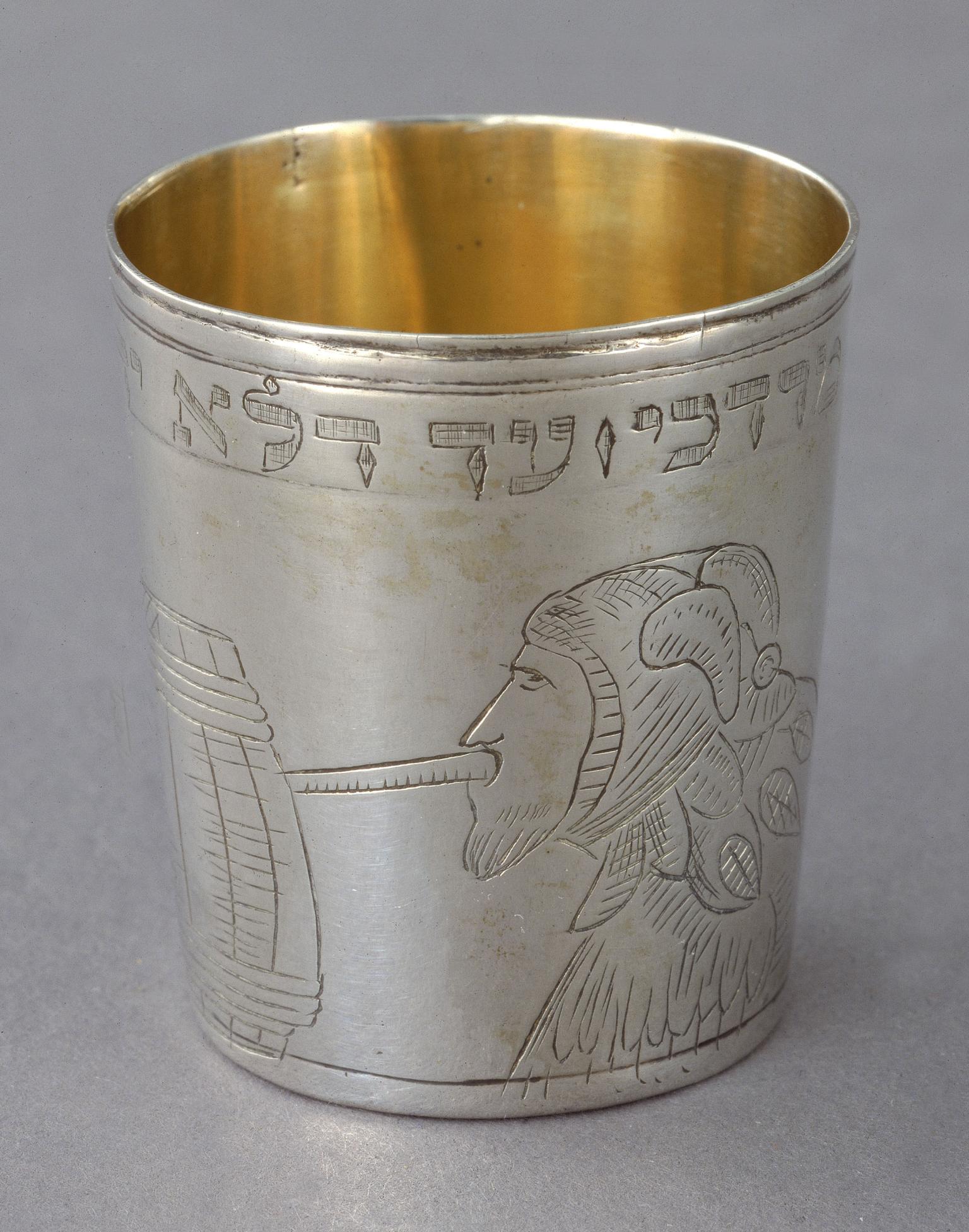 Silver cup engraved with a person in profile wearing a jester hat drinking out of a barrel. 