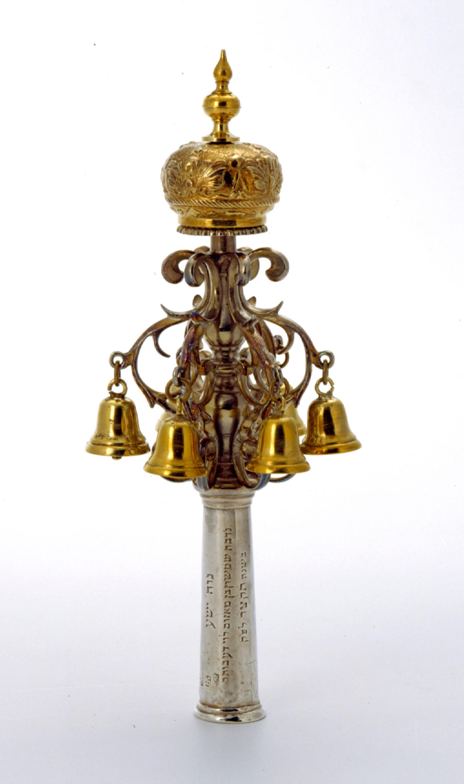 Finial with Hebrew inscription on its base, bells, and crown on top.