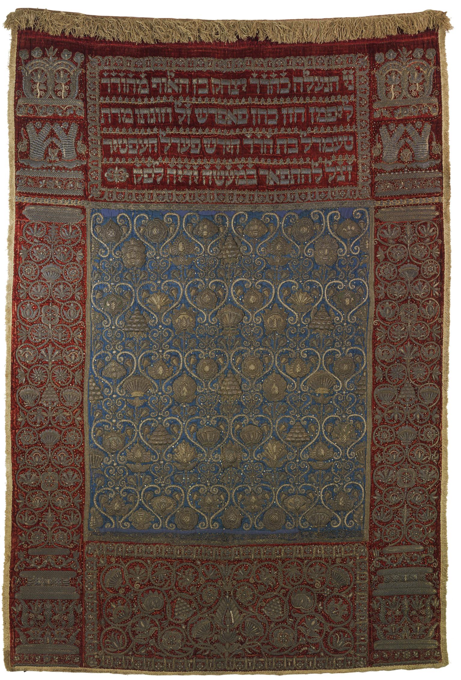 Cloth embroidered with floral border, Hebrew text across the top, and repeating motif in center. 