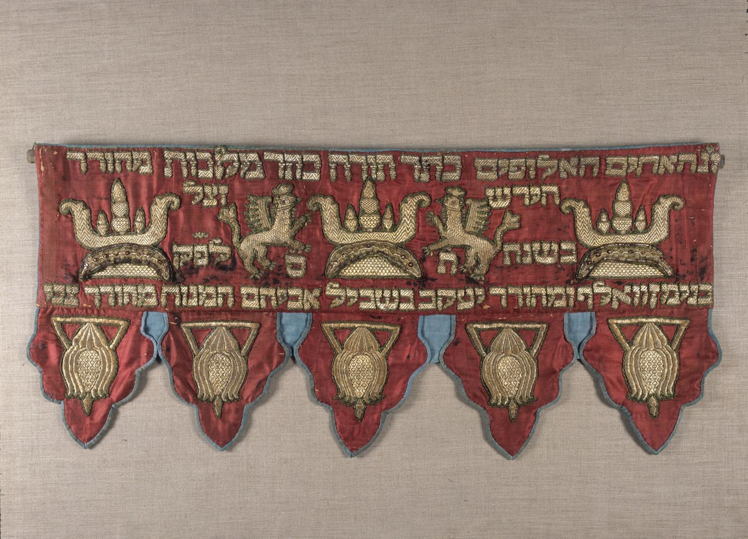 Short curtain embroidered with Hebrew text across the top with griffins and crowns. 