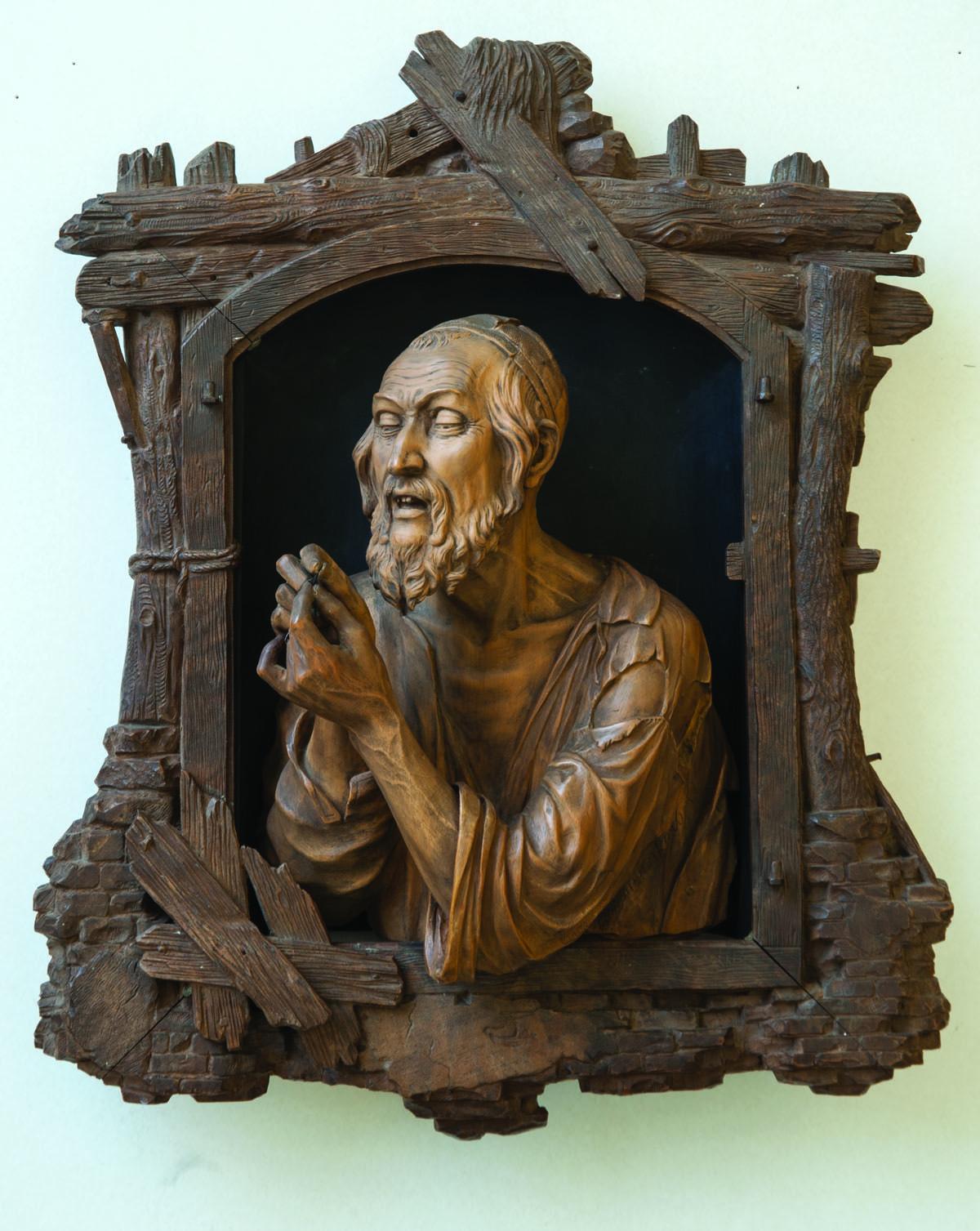 Wood-carving of a man in skullcap examining an object in his hands.