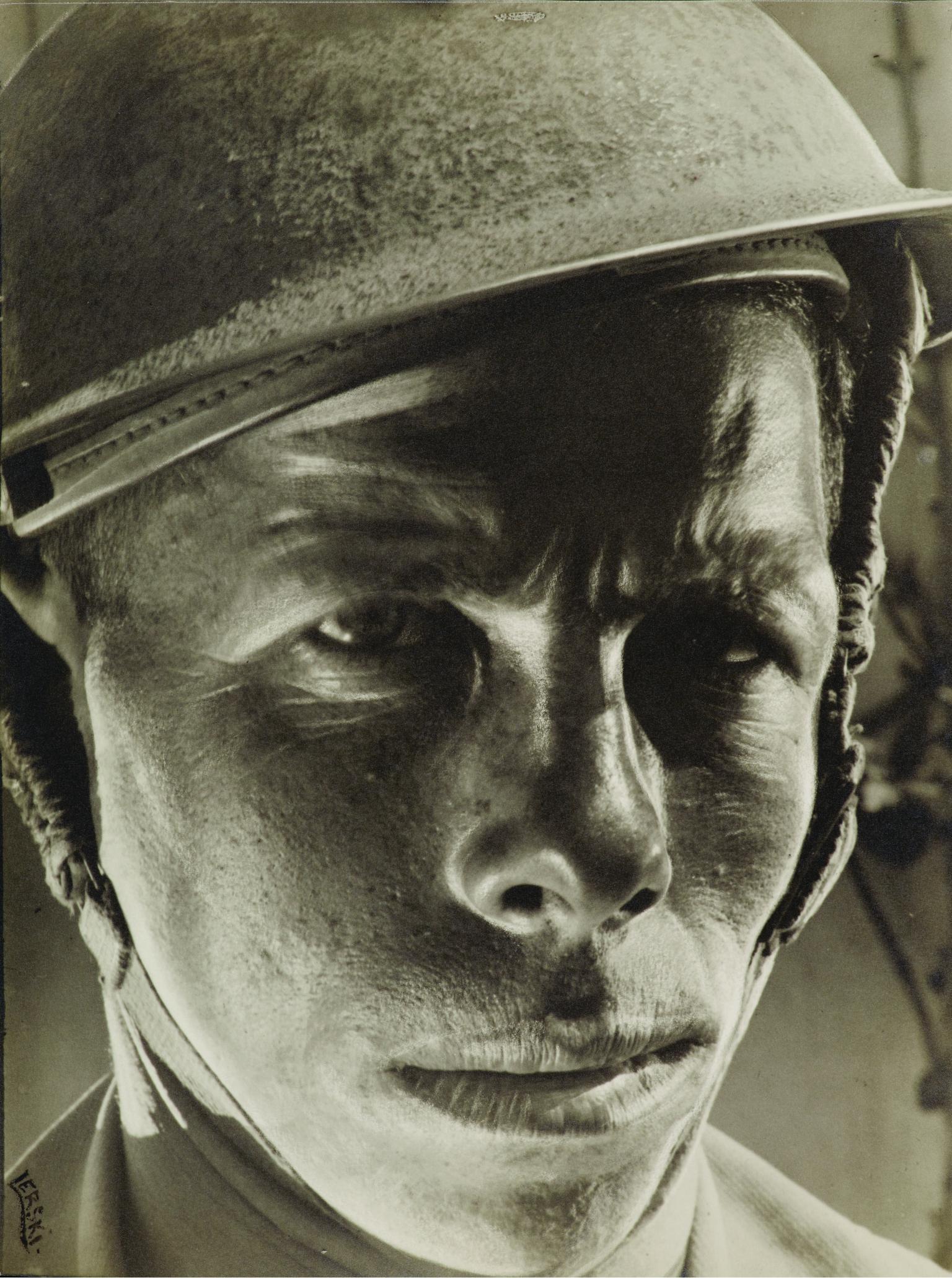 Portrait photograph of soldier wearing helmet and stern expression.