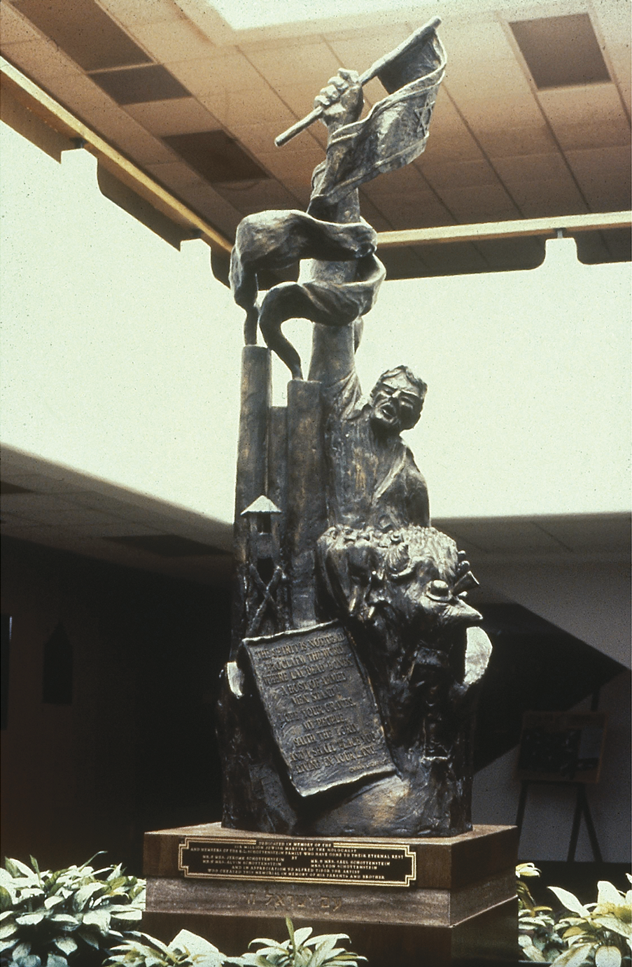 Photograph of sculpture in an atrium depicting man in labor camp with arm raised holding a flag. 