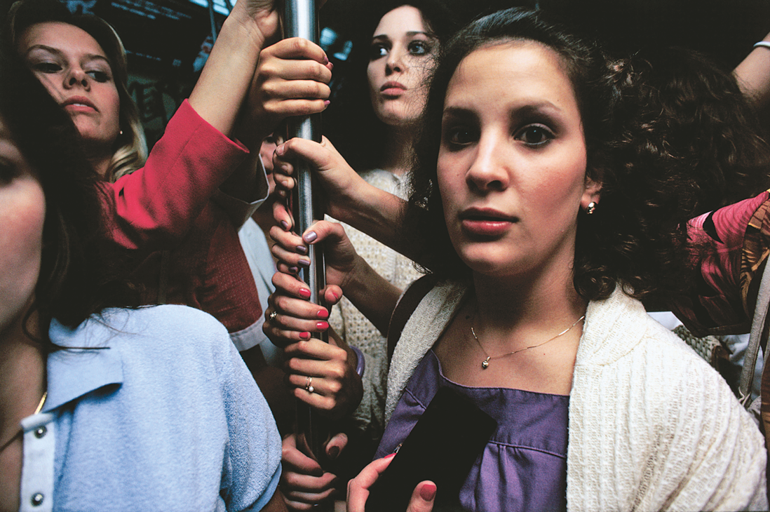 Photograph featuring women standing holding on to a subway pole. 