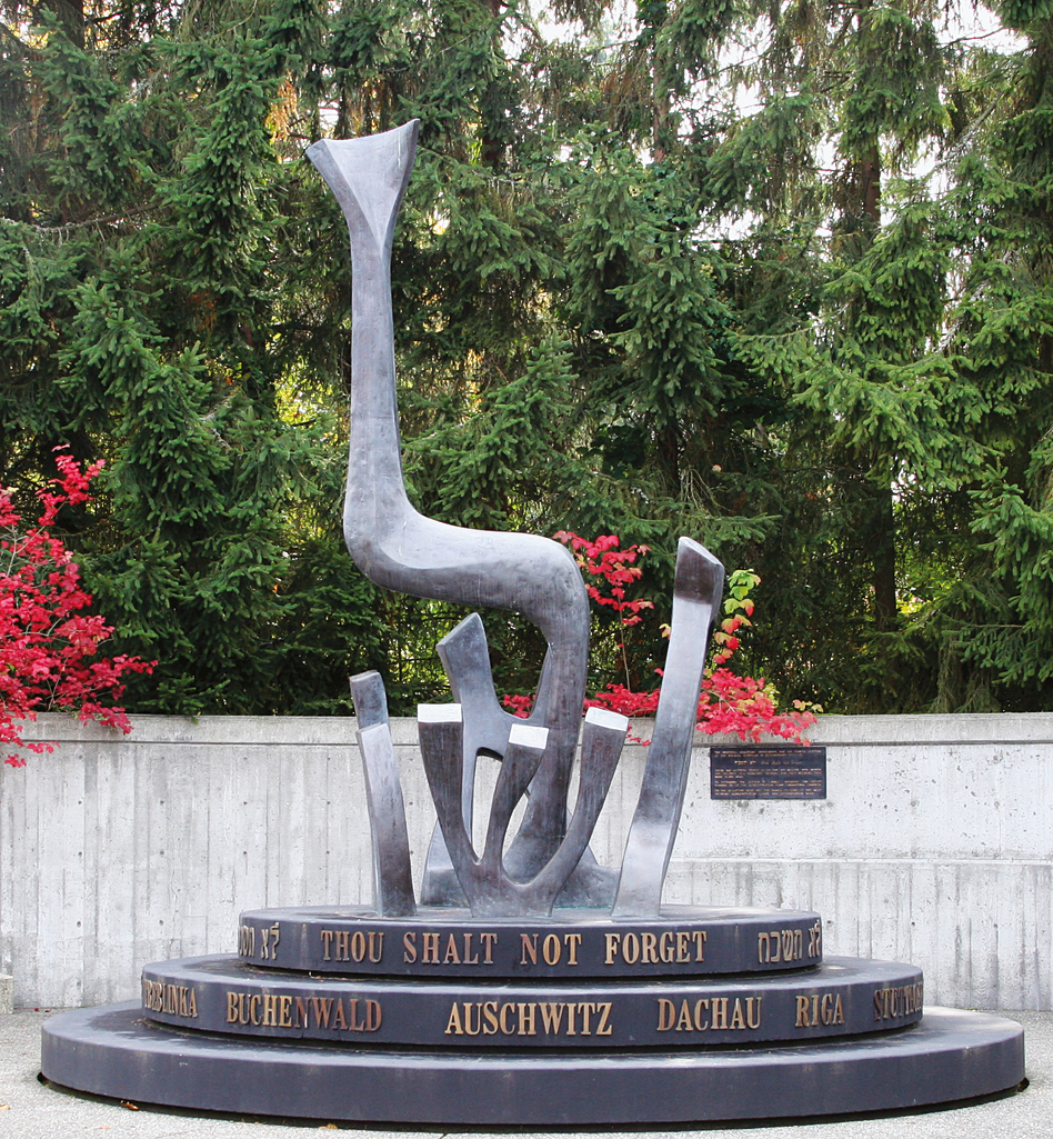 Sculpture in the shape of Hebrew letters, with a circular base with English and Hebrew words, set against a leafy backdrop. 