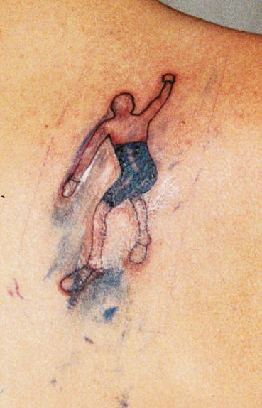 Painted bronze figurine climbing wall with no hair or shirt and silver-covered feet; tattoo of figure climbing.