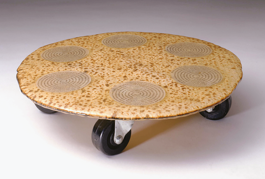 Matzah and paper in epoxy resin on wheels with six spirals made of typeset text on top of matzah. 