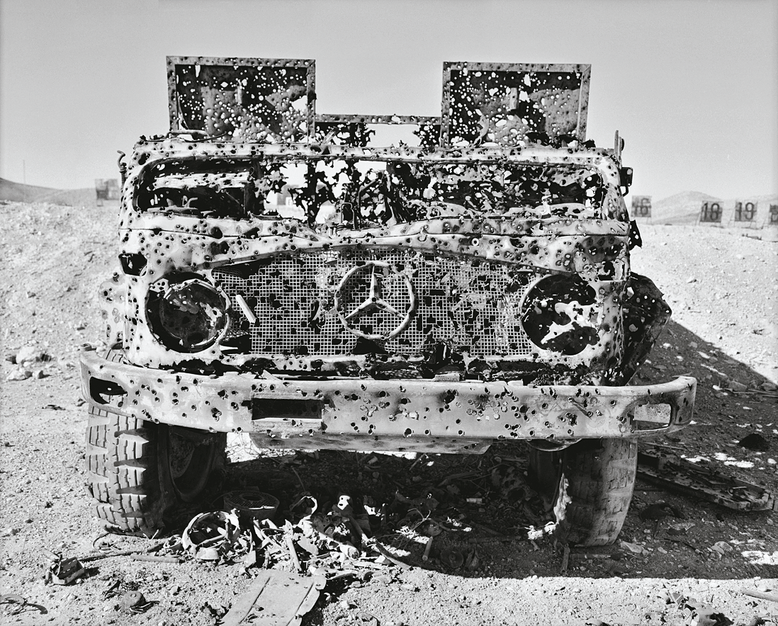 Photograph of bullet-riddled truck in desert. 