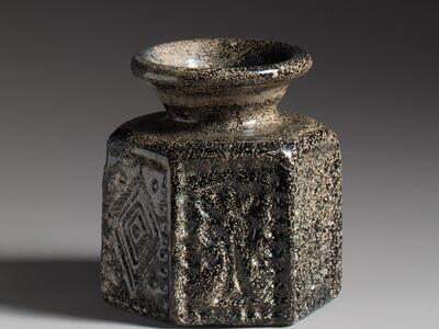 Photo of a dark glass vase with a wide, flared rim and hexagonal base, featuring geometric patterns.
