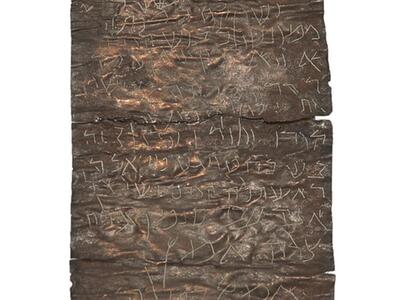 Oblong piece of metal with rough surface and Hebrew script etched into it.